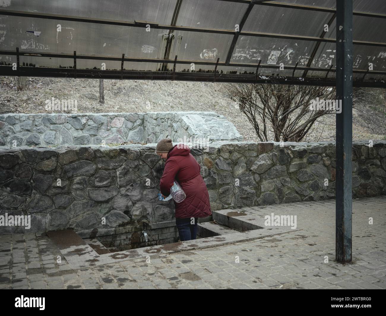 A woman fills drinking water at a public well. In the northern and eastern neighbourhoods of Kharkiv, many residential buildings have been destroyed Stock Photo