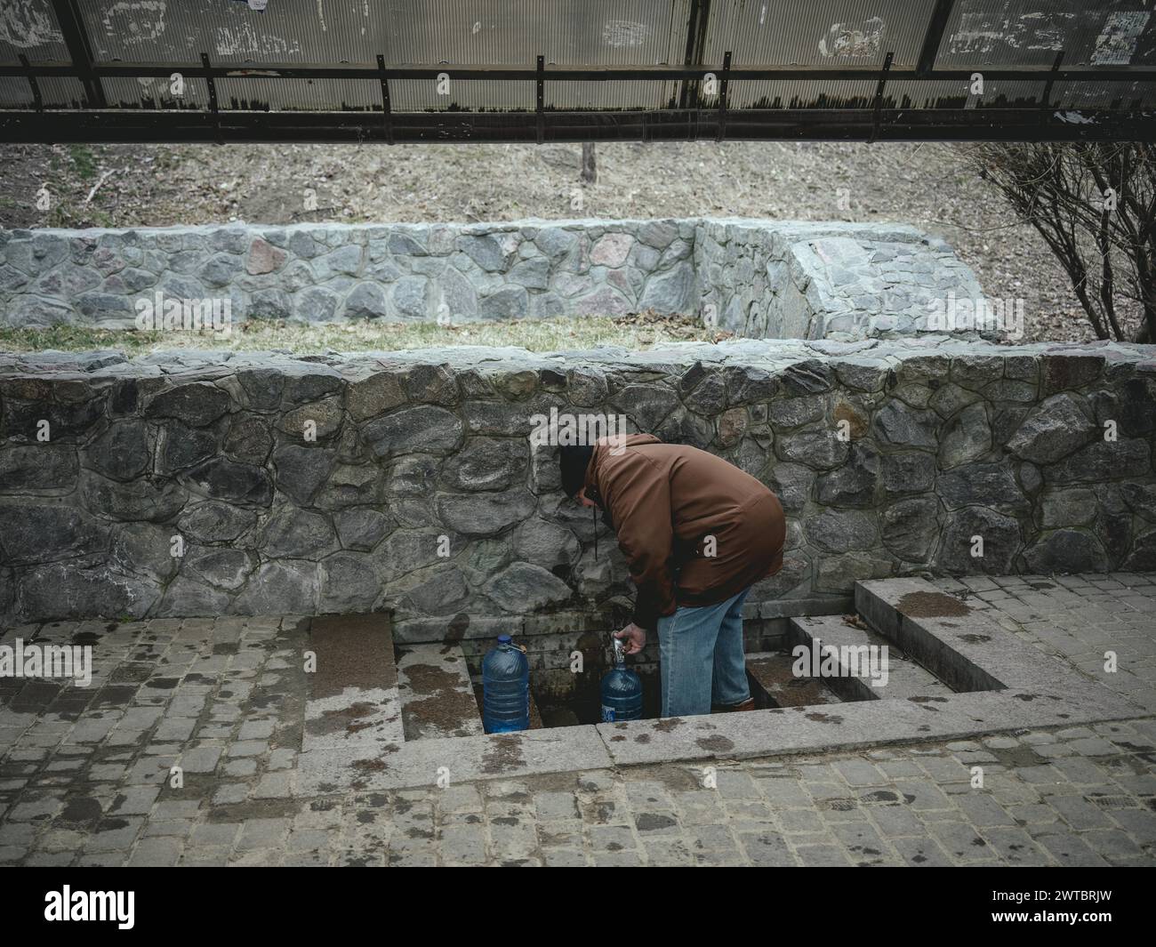 A man fills drinking water at a public well. In the northern and eastern neighbourhoods of Kharkiv, many residential buildings have been destroyed Stock Photo