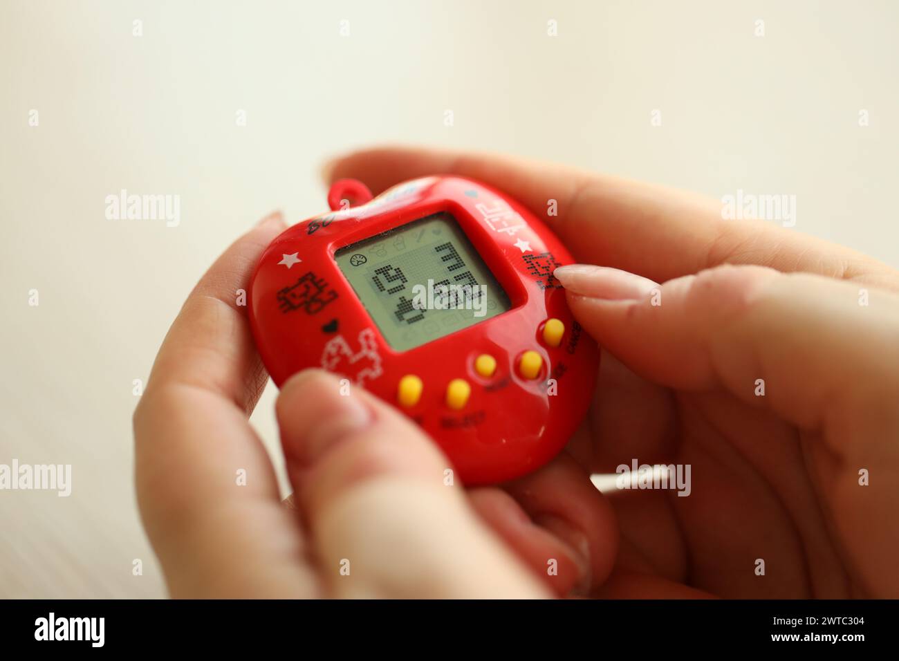 KYIV, UKRAINE - MARCH 9, 2024 Retro pet keychain game tamagotchi in red plastic case in female hands close up Stock Photo