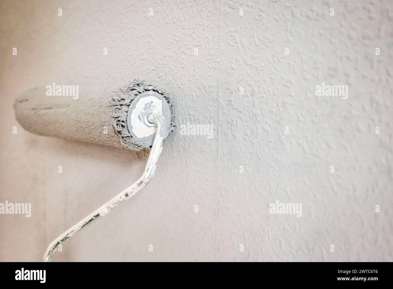 Paint roller extendable pole over painted woodchip wallpaper wall