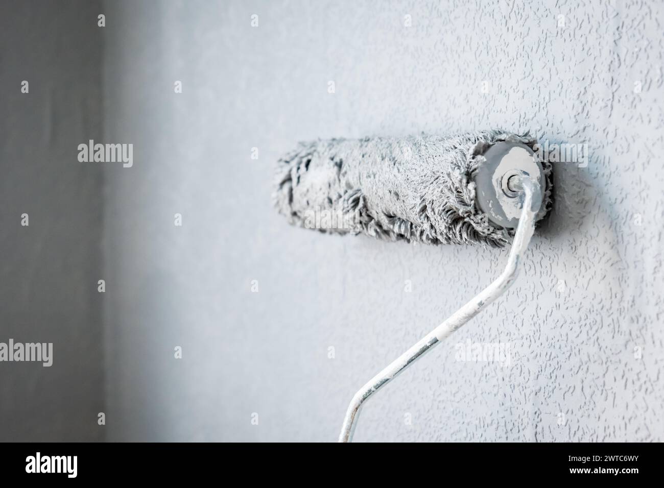 Paint roller extendable pole over painted woodchip wallpaper wall