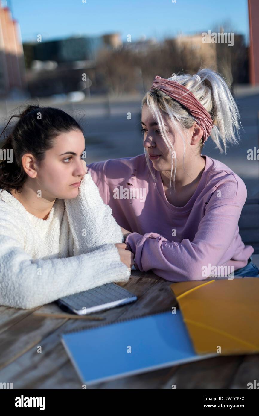 Two individuals sit together in an outdoor setting, interacting and sharing ideas. They are surrounded by notebooks and an electronic device, indicati Stock Photo
