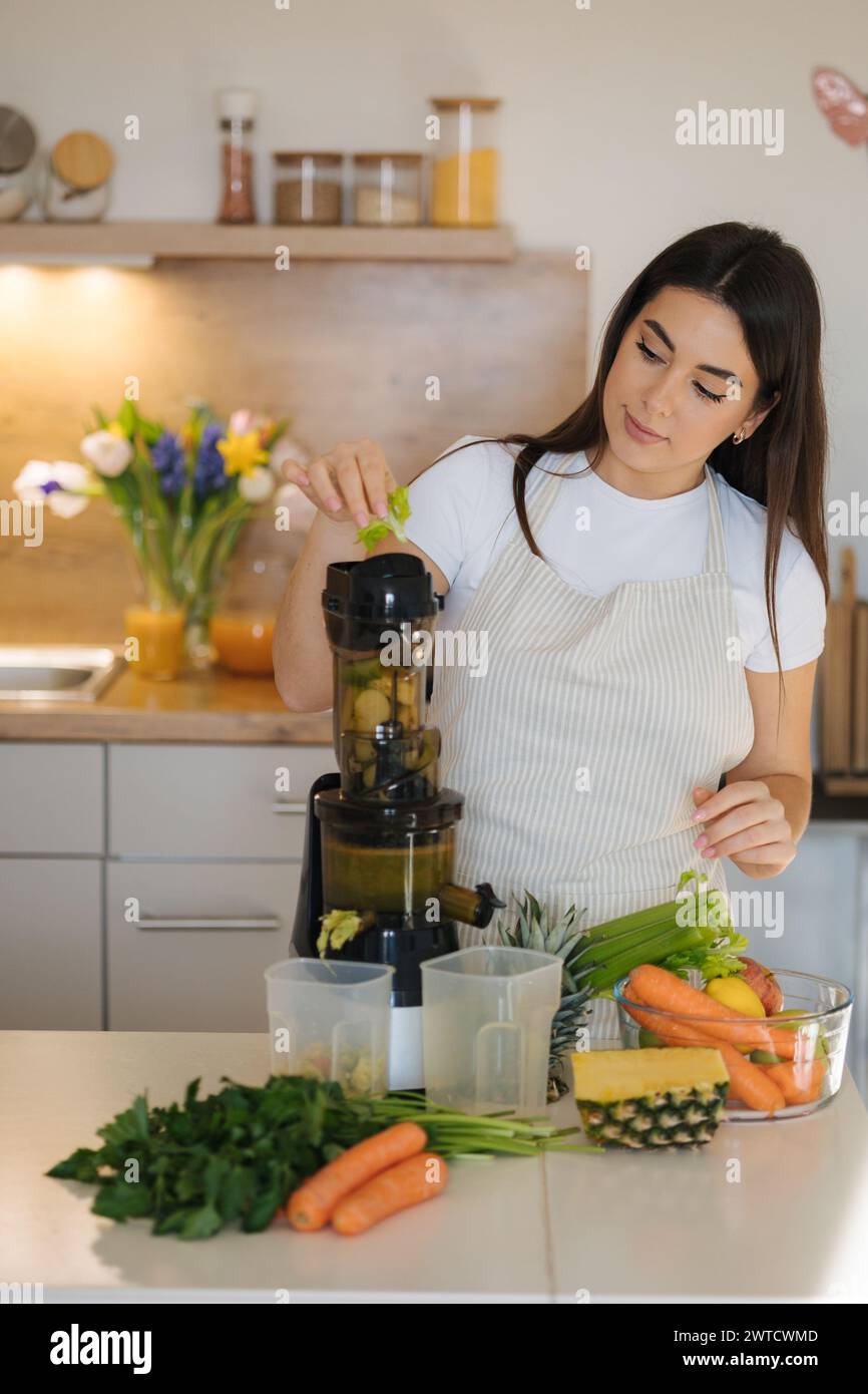 Young woman put celery into juicer. Process of making healthy drink