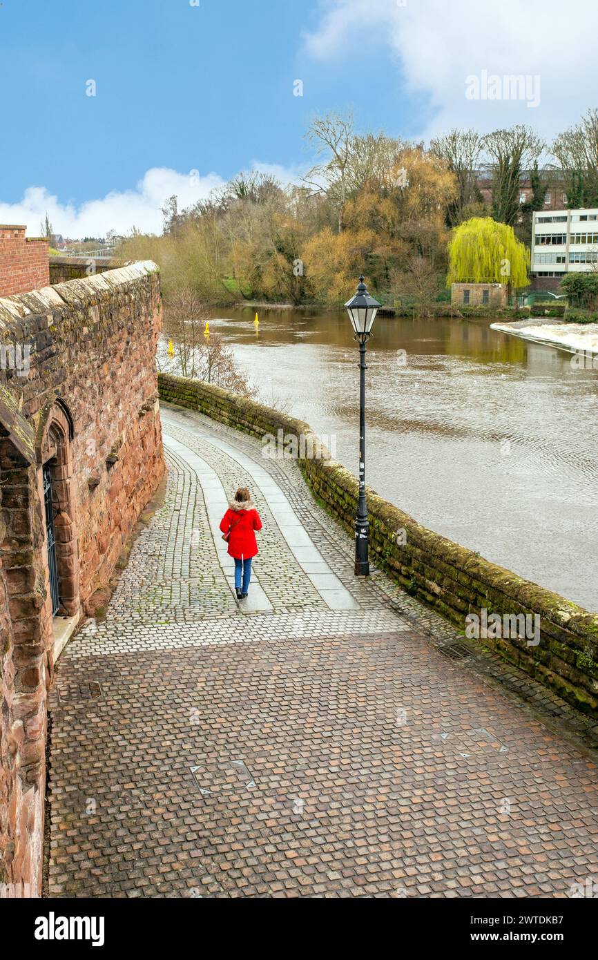 Woman in a red coat walking alongside the Roman walls in the Cheshire city of Chester England UK with the river Dee running alongside Stock Photo