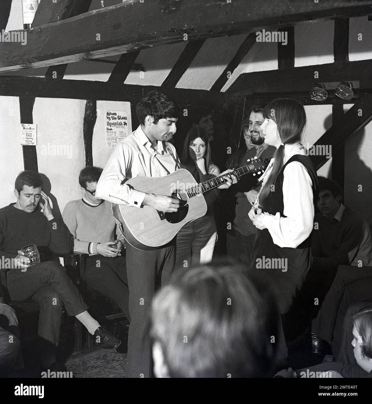 1970, historical, folk music, a musican playing the guitar and a female singer performing inside an old pub, England,UK. Stock Photo