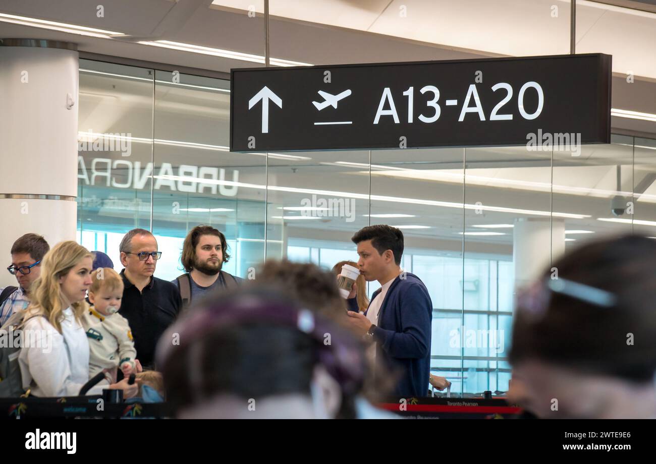 TORONTO, CANADA - 03 10 2024: A black sign with white letters of the gate number with a group of travelers under it waiting for boarding in a crowded Stock Photo