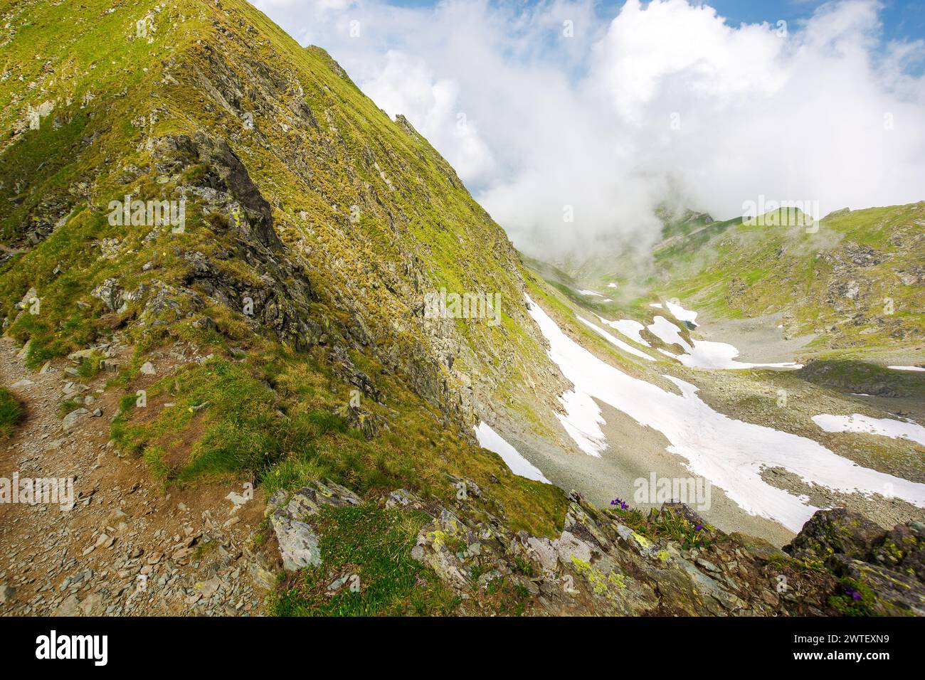 landscape of transylvania alps in summer. spots of snow among grass on the rocky hills of fagaras range beneath a sky with clouds. popular travel dest Stock Photo