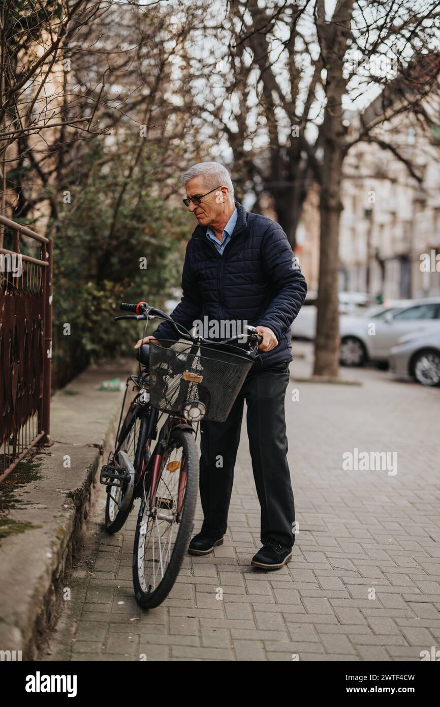 An active elderly man walks with his bicycle on a paved street, depicting urban commuting and a healthy lifestyle for seniors. Stock Photo