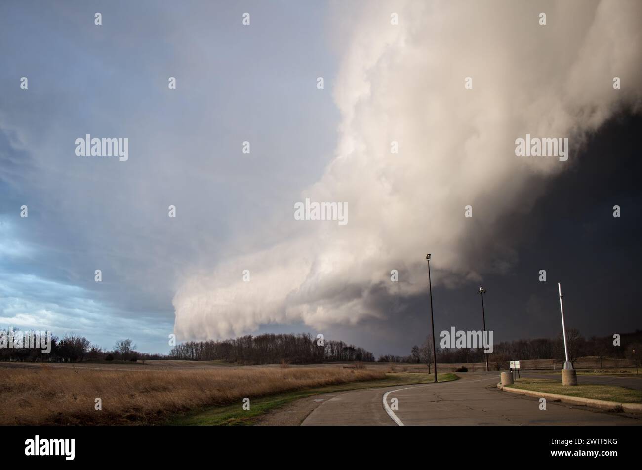 An immense shelf cloud and severe thunderstorm approaches rapidly with a road and streetlights in the foreground Stock Photo