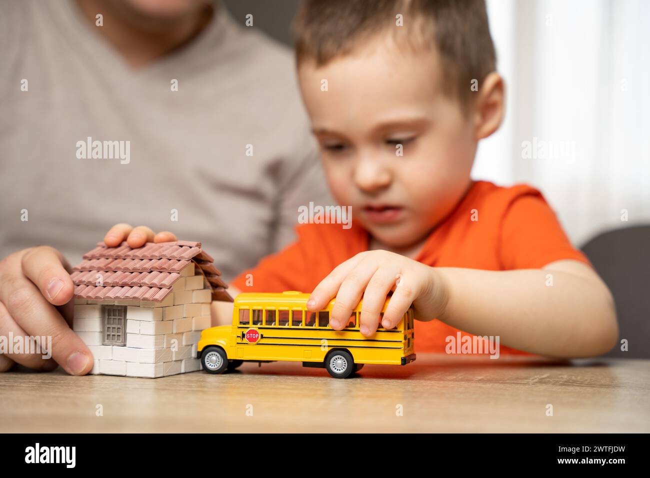 Dad and son play with a house and a school bus. Spending time with children. The concept of a happy childhood. Indoor, home Stock Photo