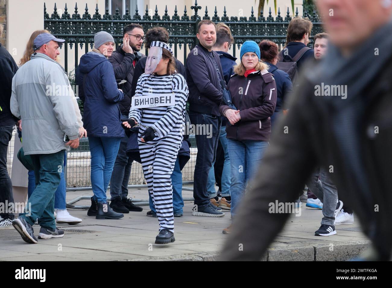 London, UK. 17th March, 2024. A protester wearing a prison outfit, Putin facemask and in handcuffs walks along the voters' queue. Thousands of voters descended on the Russian Embassy in Kensington with some voters queuing for four hours before they cast their ballot. Many waiting were seen draped in the pro-democracy blue and white flag as Yulia, the wife of the late opposition leader Alexei Navalny, urged voters to turn up in a 'Noon against Putin' protest, whilst Navalny's team asked for individuals to spoil their ballot papers. Credit: Eleventh Hour Photography/Alamy Live News Stock Photo