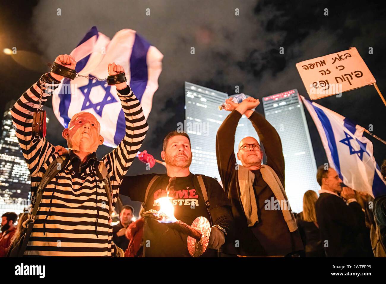 A protester dressed in a convict uniform and a Benjamin Netanyahu mask lifts his handcuffed arms in the air during a demonstration. Thousands of Israelis protest in the pouring rain calling for Prime Minister Benjamin Netanyahu's ousting. Stock Photo