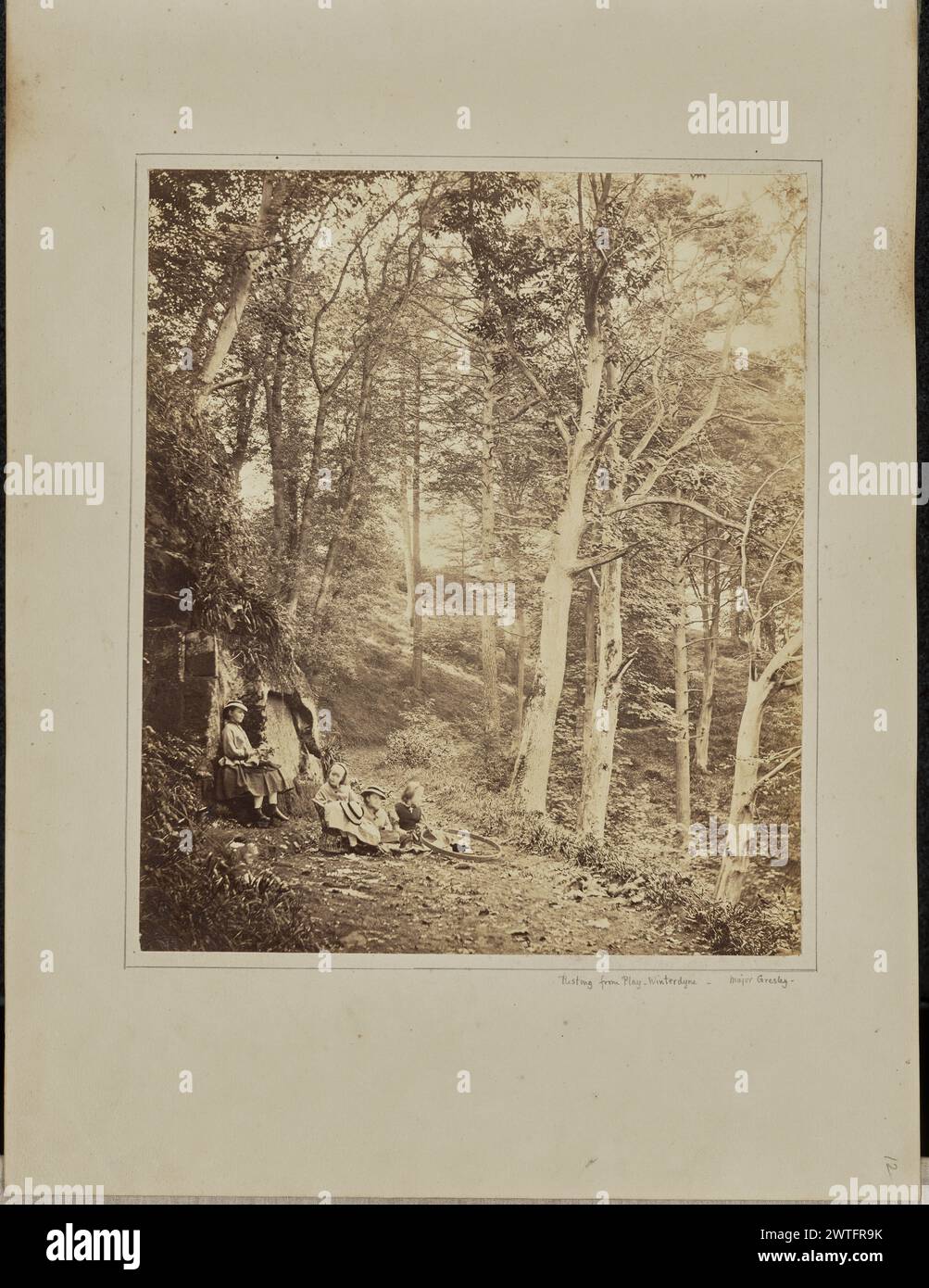 Resting from Play. Winterdyne. Major F. Gresley, photographer (British, 1807 - 1880) about 1862–1868 A woman and three children gathered in a clearing in the woods. The woman is sitting with her back to a small structure resembling a hut. Two of the children are sitting on the ground, while the third sits in a small wicker chair. (Recto, mount) lower right, below image, pencil in Sir John Joscelyn Coghill's hand: 'Resting from Play. Winterdyne. [space] Major Gresley.'; lower right, pencil: '12'; Stock Photo