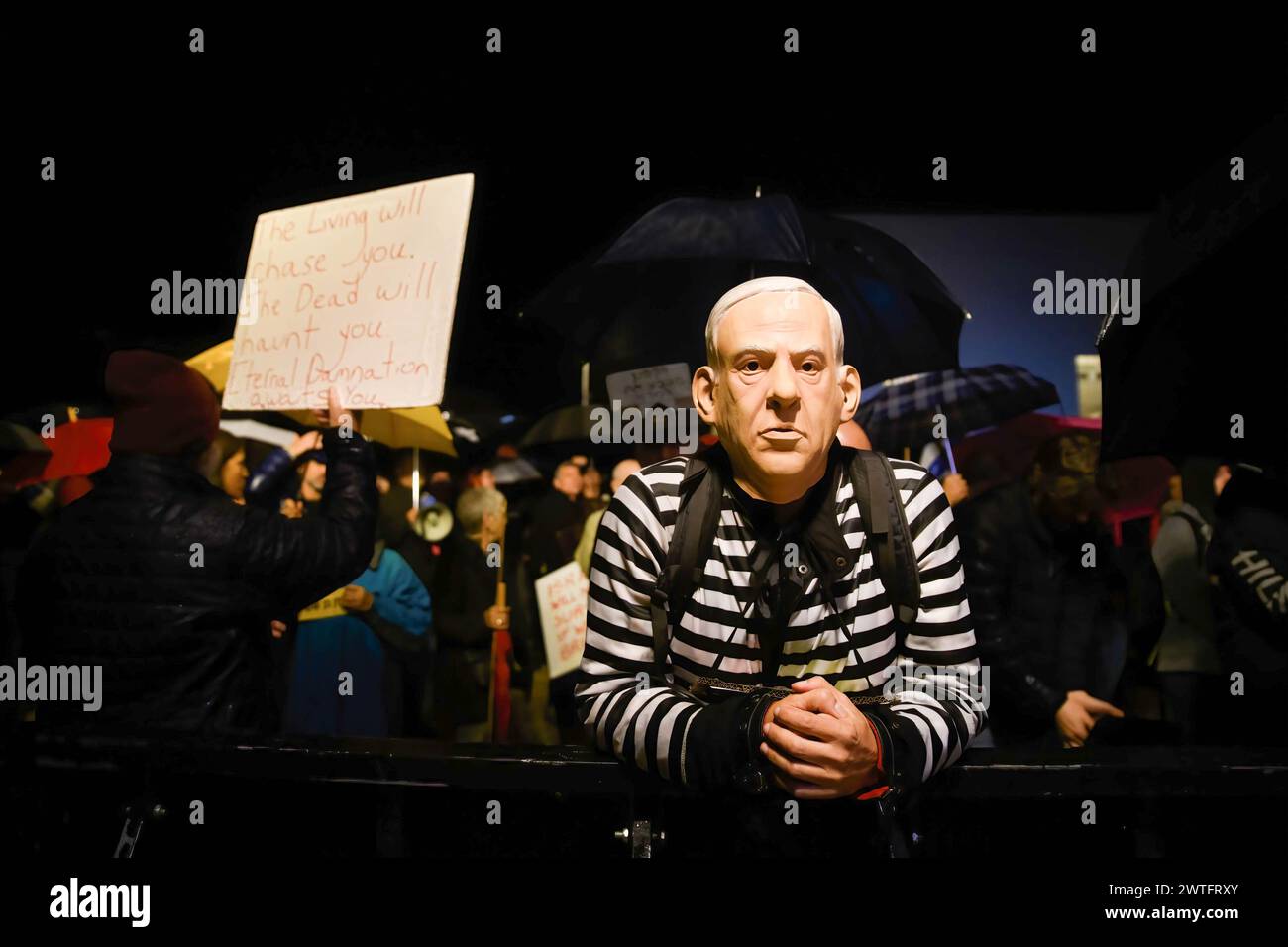 Tel Aviv, Israel. 23rd Dec, 2023. A protestor in a convict uniform wears a Benjamin Netanyahu mask next to a sign that reads Ã¬The living will chase you. The dead will haunt you. Eternal damnation awaits youÃ® during a demonstration attended by thousands under pouring rain calling for Prime Minister Benjamin Netanyahu ousting. Tel Aviv, Israel. Dec 23th 2023. (Matan Golan/SOPA Images).during the demonstration. Thousands of Israelis protest in the pouring rain calling for Prime Minister Benjamin Netanyahu's ousting. (Credit Image: © Matan Golan/SOPA Images via ZUMA Press Wire) EDITORIAL U Stock Photo