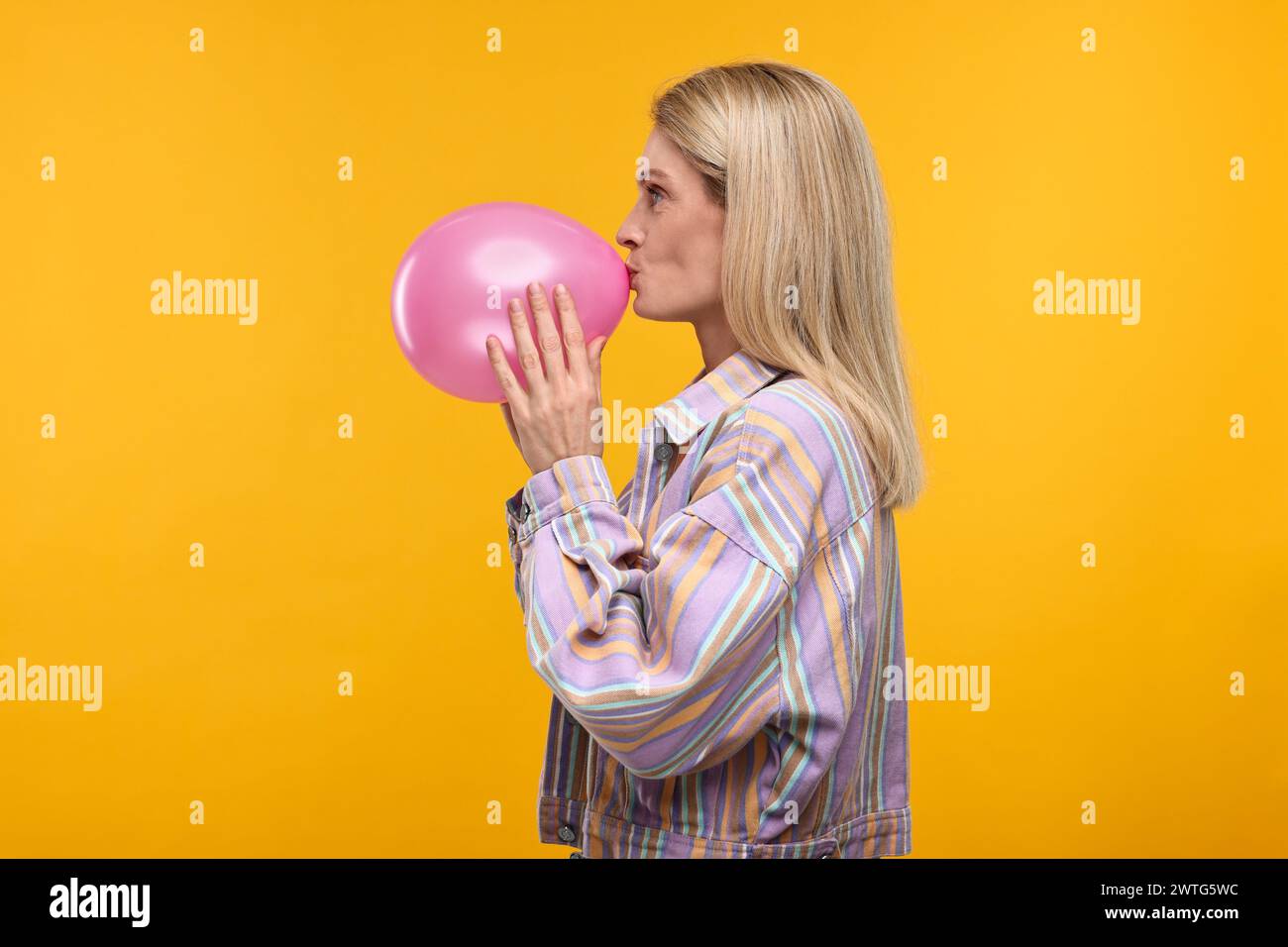 Woman blowing up balloon on yellow background Stock Photo