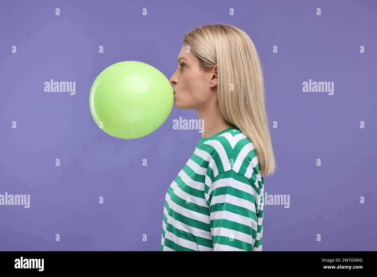 Woman blowing up balloon on violet background Stock Photo