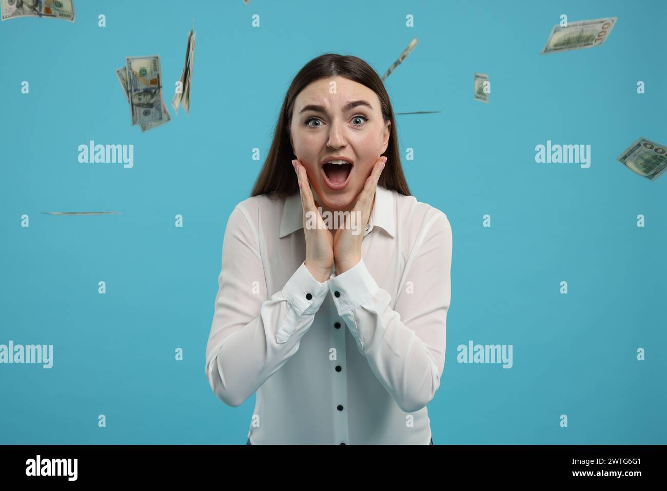 Excited woman under money shower on light blue background Stock Photo