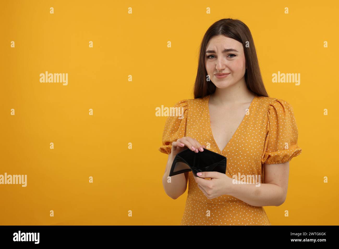 Sad woman showing empty wallet on orange background, space for text ...