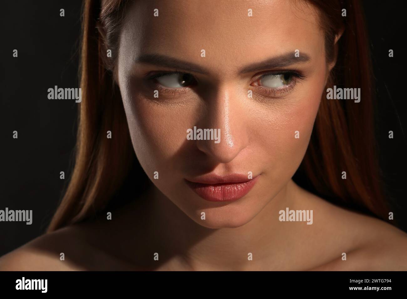 Evil eye. Young woman with scary eyes on black background, closeup Stock Photo