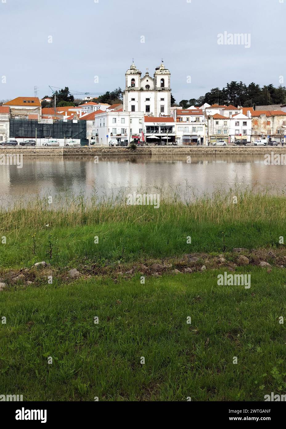 View of the town historic center across the River Sado, grassy left bank of the river in the foreground, Alcacer do Sal, Portugal Stock Photo