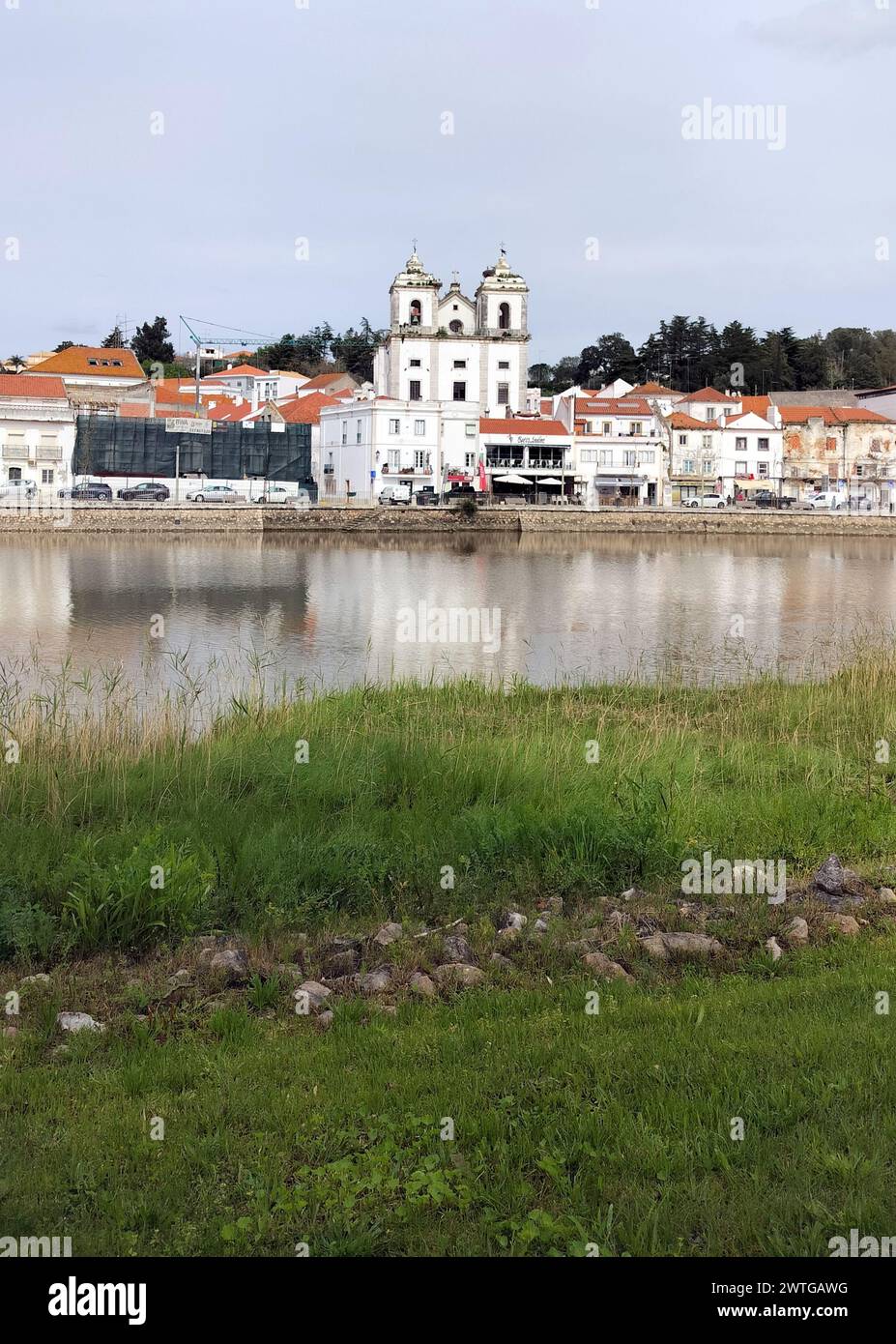 View of the town historic center across the River Sado, grassy left bank of the river in the foreground, Alcacer do Sal, Portugal Stock Photo