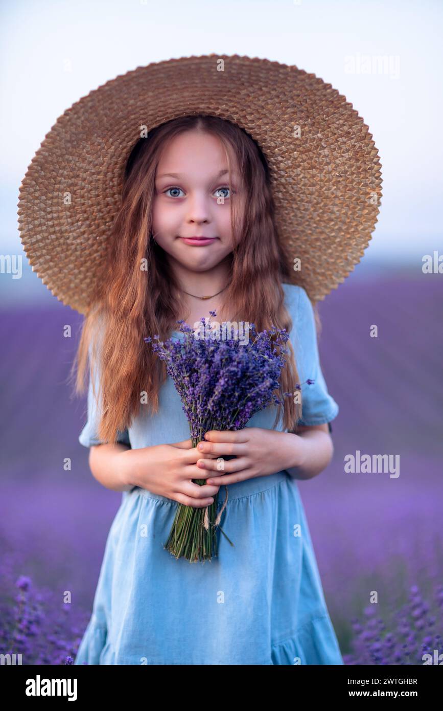Girl lavender field in a blue dress with flowing hair in a hat stands ...
