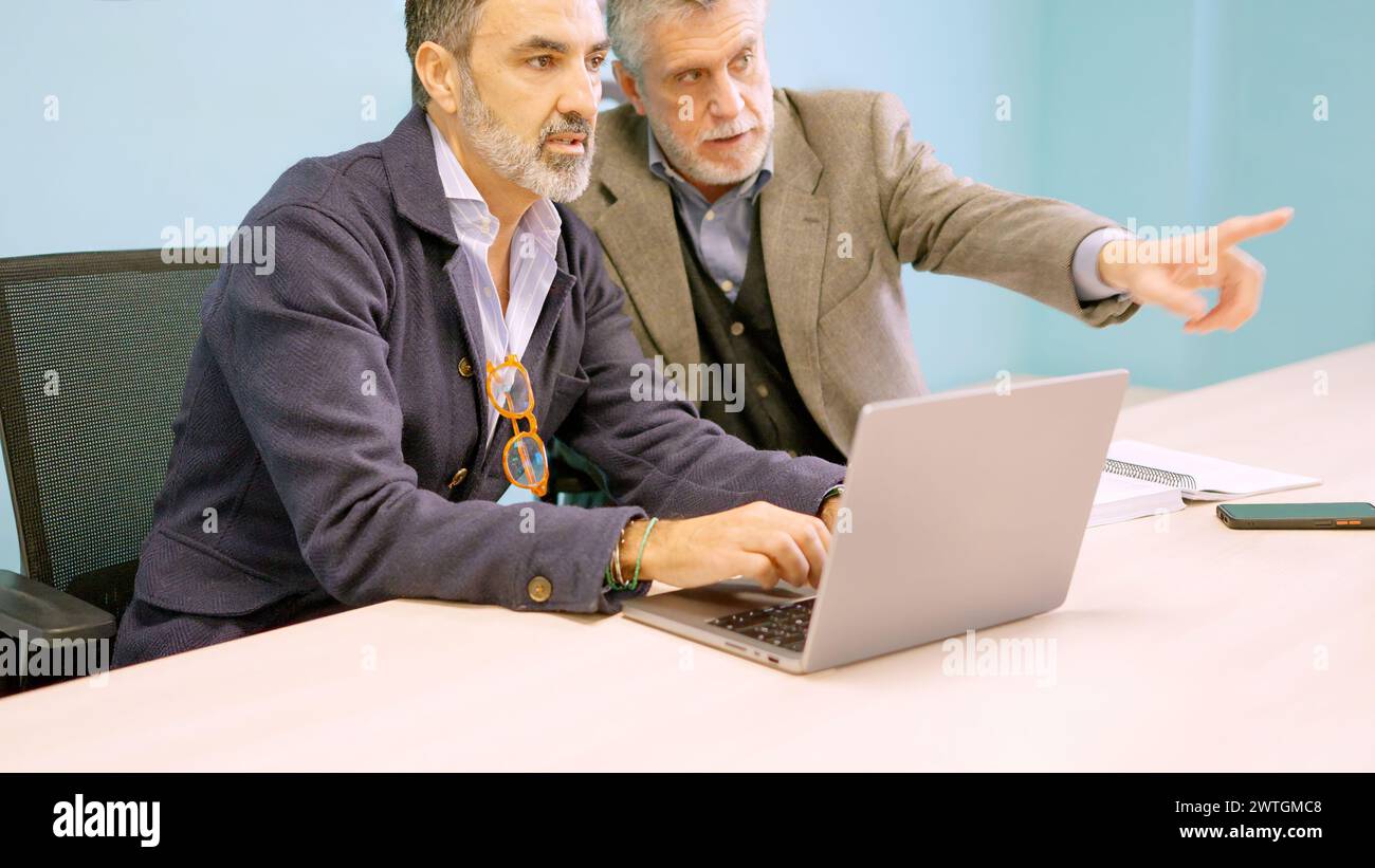 Partners discussing which workers they will dismiss while using laptop Stock Photo