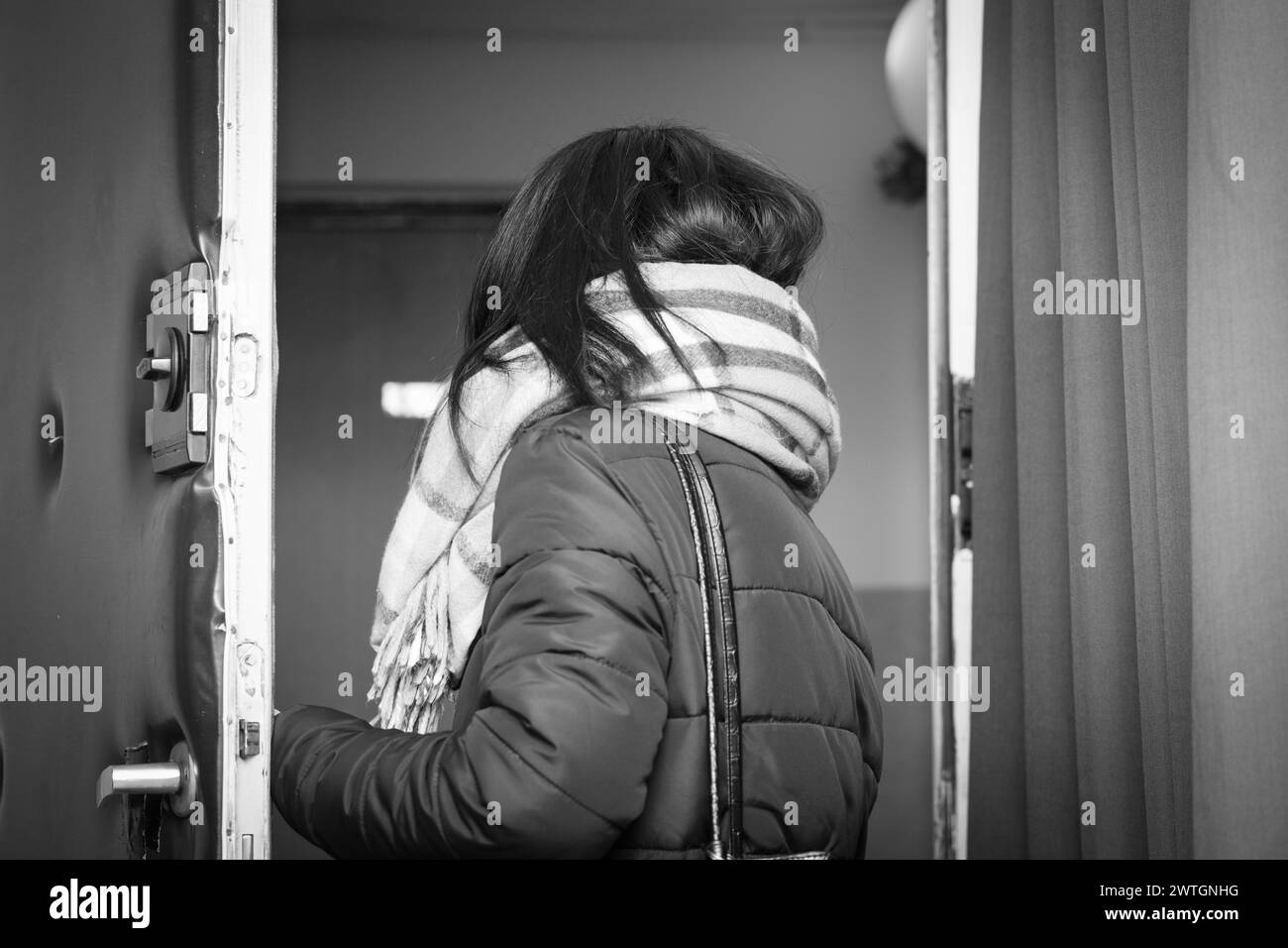 Woman wearing a shawl, in the doorway leaving the flat. Black and white. Stock Photo