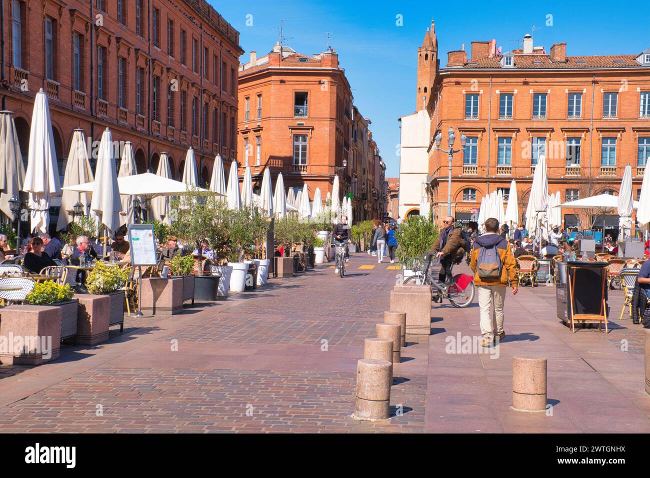 Toulouse Haute Garonne France 03.13.24 place du Capitole.Market day. Alfresco dining. Grand historic red brick buildings. Arches and shops. Stone balu Stock Photo