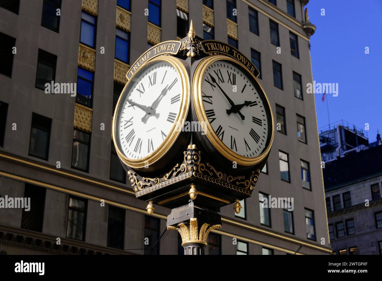 Illuminated golden street clock at night with a prominent building in the background, Manhattan, New York City, New York, USA, North America Stock Photo
