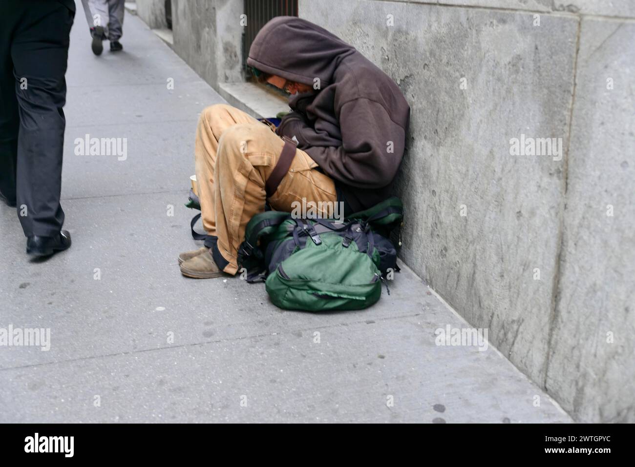 A homeless person sleeps curled up on a pavement with a green rucksack next to him, Manhattan, New York City, New York, USA, North America Stock Photo