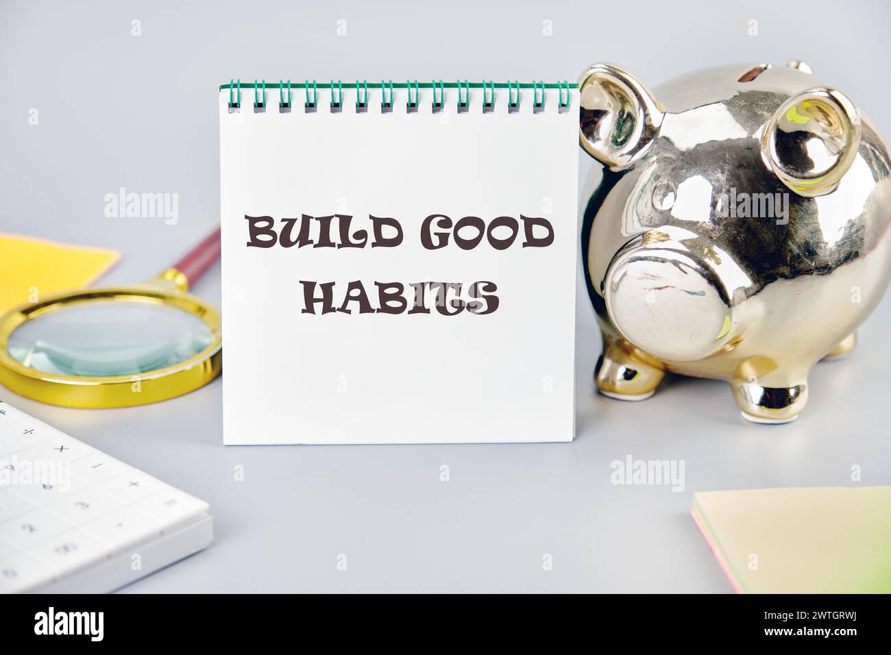 BUILD GOOD HABITS motivational concept text on a white notebook on a gray background near a piggy bank, a calculator and stickers Stock Photo
