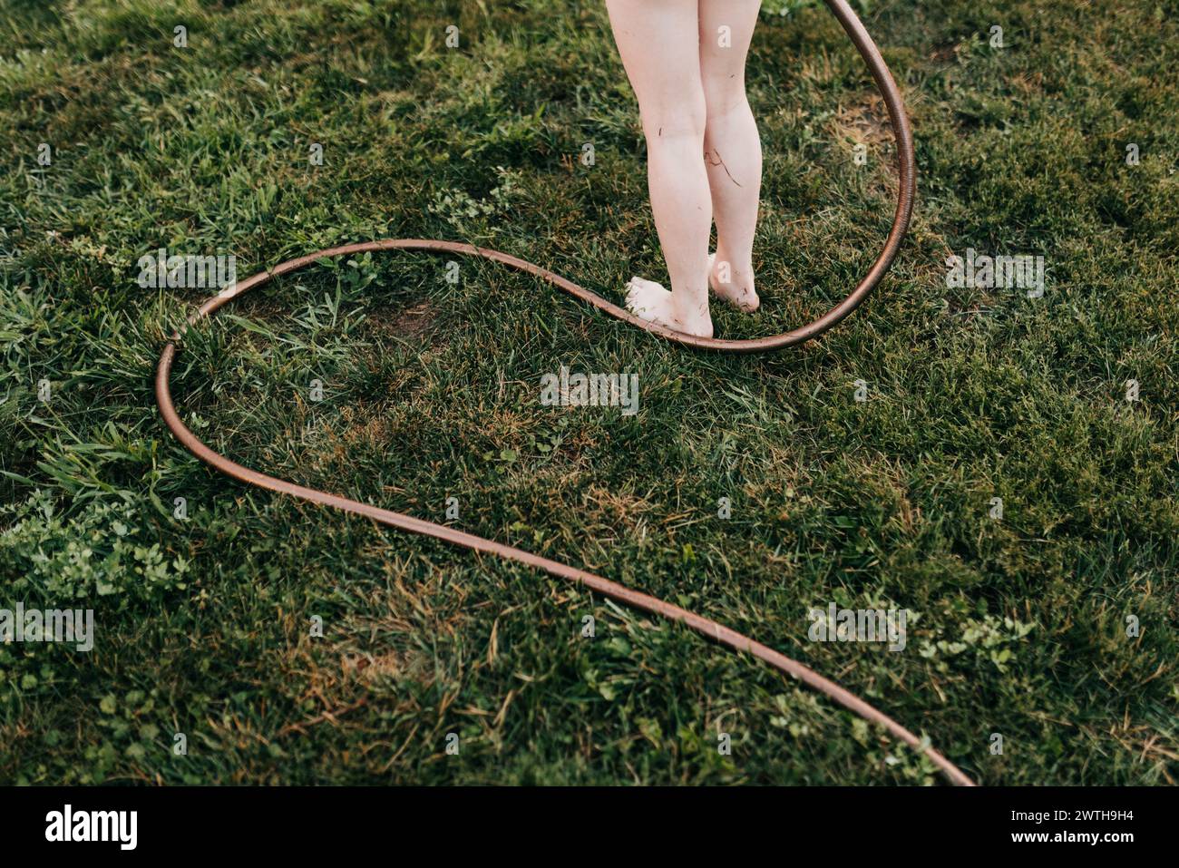 Garden hose trails through grass around young child's feet Stock Photo