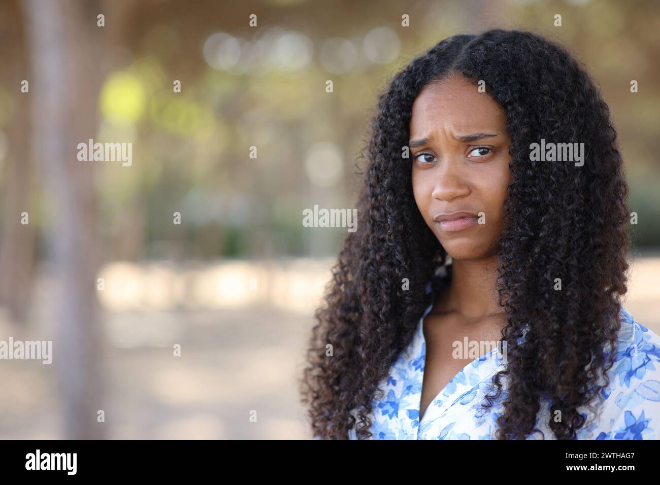 Disappointed black woman looking at camera standing in a park Stock Photo