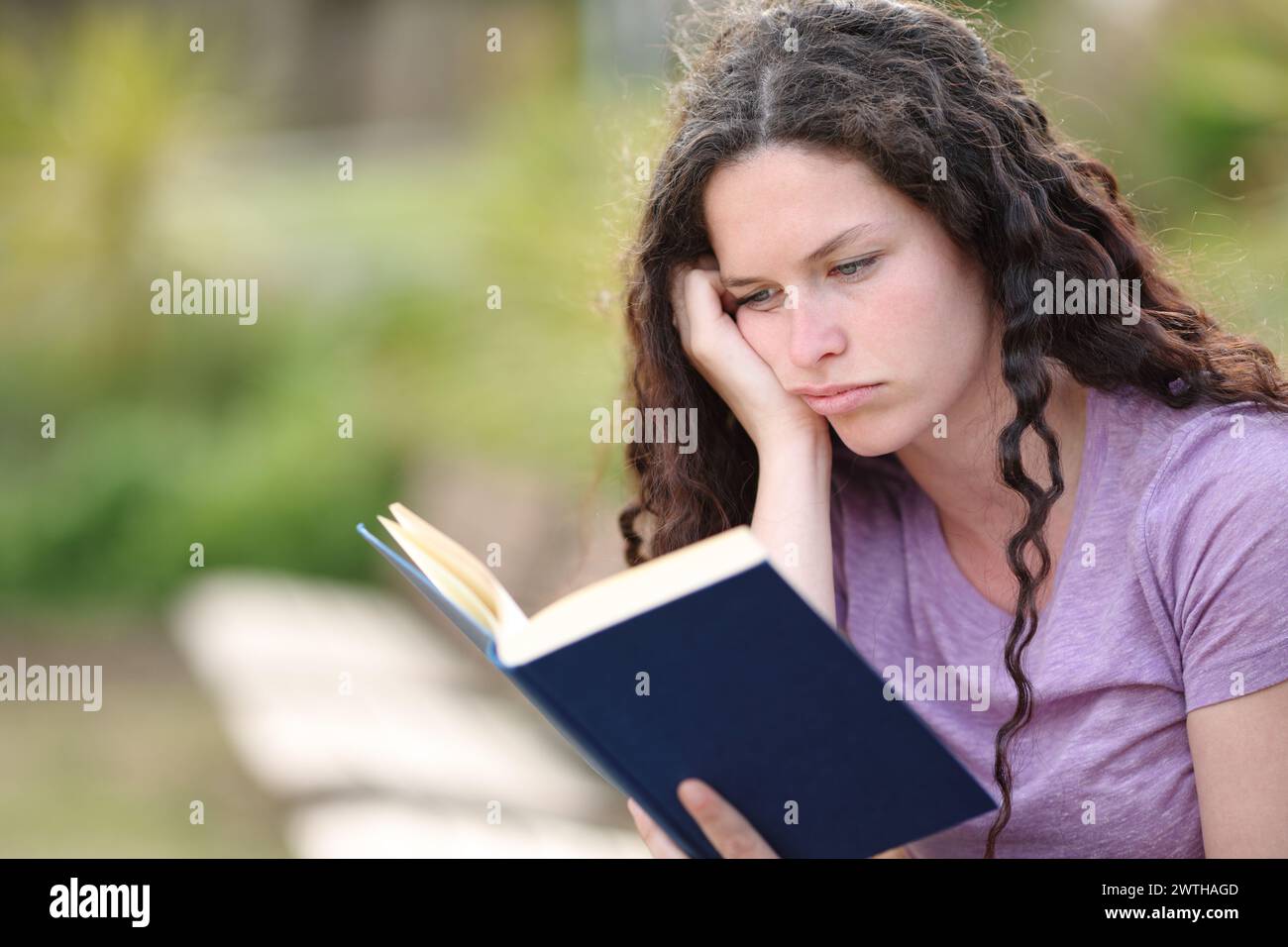 Bored woman reading a paper book sitting in a park Stock Photo