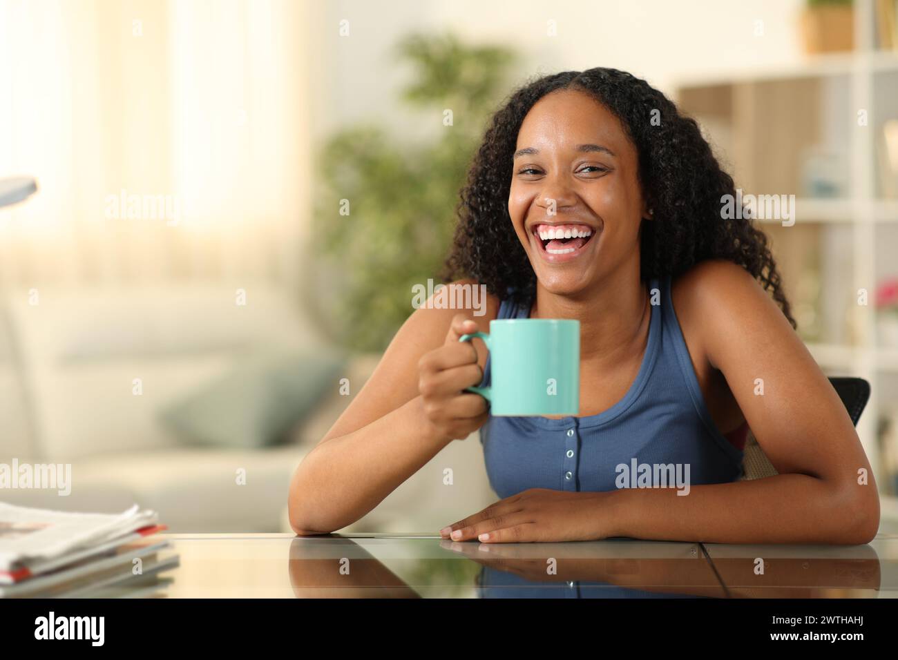 Happy black woman drinking and laughing looking at you at home Stock Photo