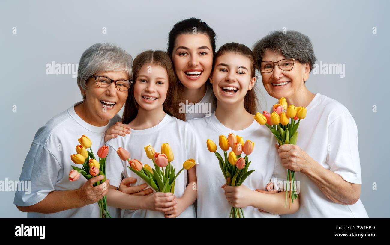 Happy mother's day! Children daughters are congratulating mom and grandmothers giving them flowers tulips. Family smiling on light grey background. Stock Photo