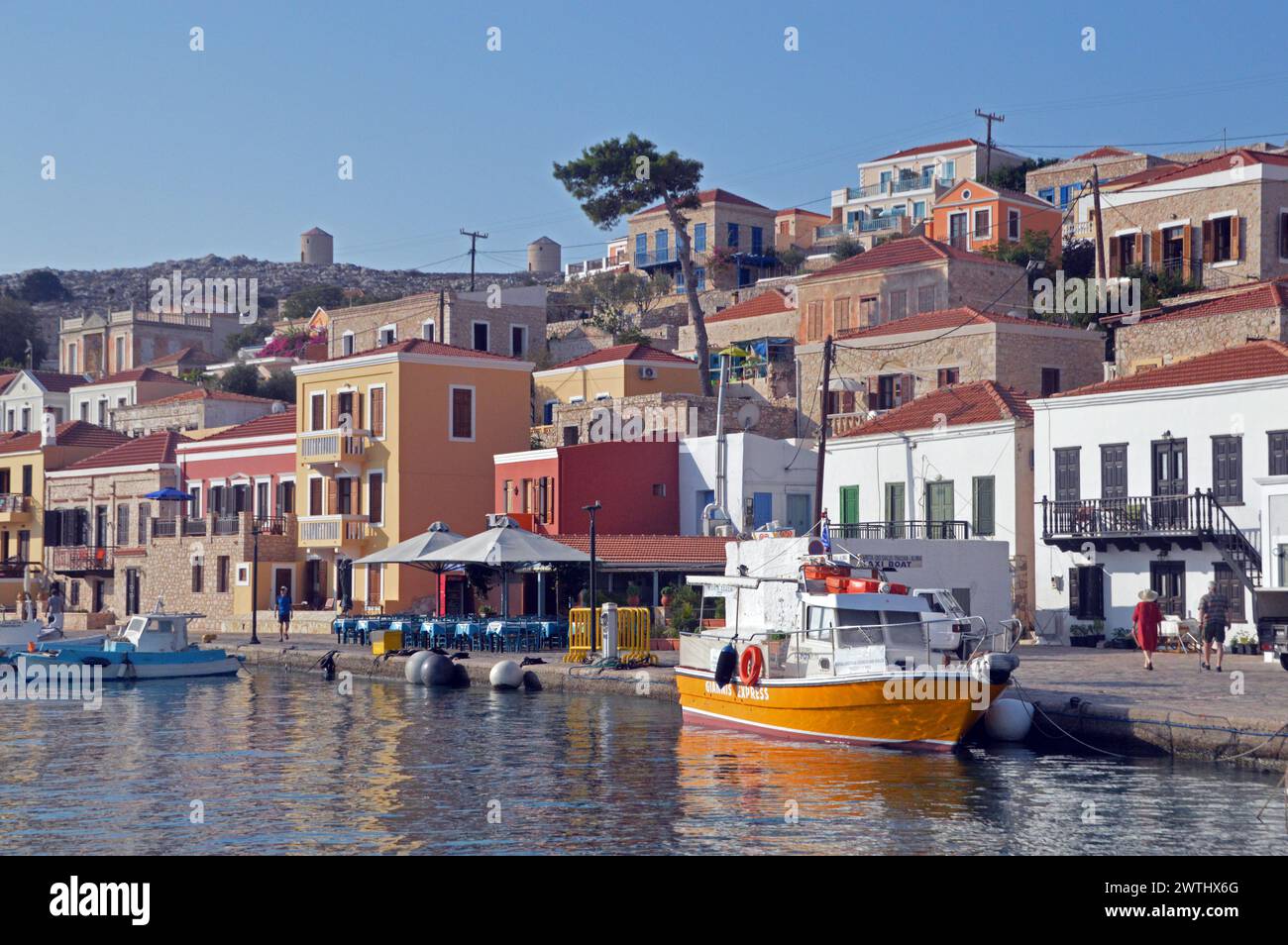 Greece, Island of Chalki:  quayside, with day-tripper motor launch and houses in terraces. Stock Photo