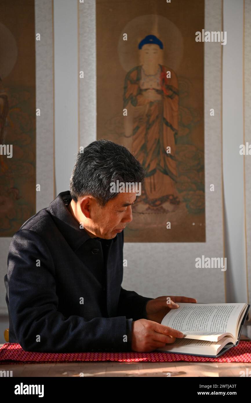 (240318) -- ZHANGZI, March 18, 2024 (Xinhua) -- Zhang Yufei reads a book at his home near Faxing Temple in Zhangzi County, north China's Shanxi Province, March 12, 2024. Faxing Temple, with a history of more than 1,000 years, is nestled on Cuiyun Mountain of Zhangzi County. In 1988, the temple was listed as a national key cultural relics protection site. Zhang Yufei, a cultural relics guardian, has worked at the temple since 1993 when he was 21. Zhang initially took on the temple's daily maintenance. He gradually took an interest in the research of the relics at the temple and began to le Stock Photo
