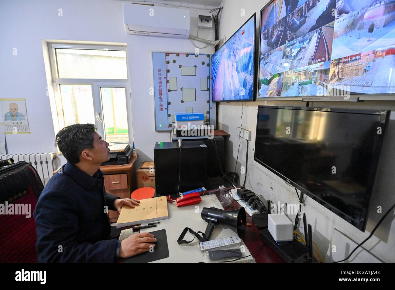 (240318) -- ZHANGZI, March 18, 2024 (Xinhua) -- Zhang Yufei watches monitors in Faxing Temple in Zhangzi County, north China's Shanxi Province, March 12, 2024. Faxing Temple, with a history of more than 1,000 years, is nestled on Cuiyun Mountain of Zhangzi County. In 1988, the temple was listed as a national key cultural relics protection site. Zhang Yufei, a cultural relics guardian, has worked at the temple since 1993 when he was 21. Zhang initially took on the temple's daily maintenance. He gradually took an interest in the research of the relics at the temple and began to learn cultur Stock Photo
