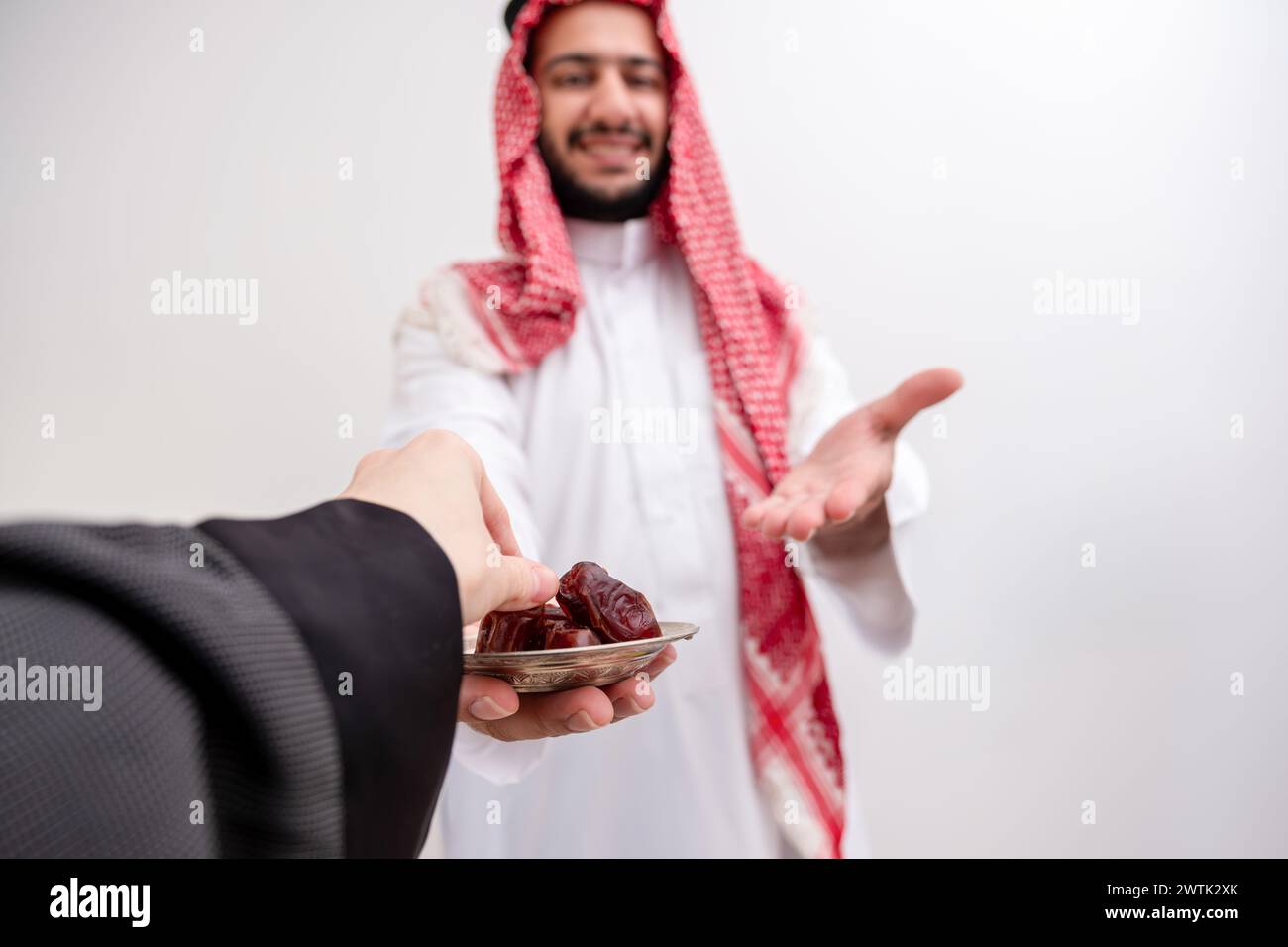 arabic man holding dates represents hospitality and generosity wearing kandura with keffiyeh on isolated white background for eid celebrations Stock Photo