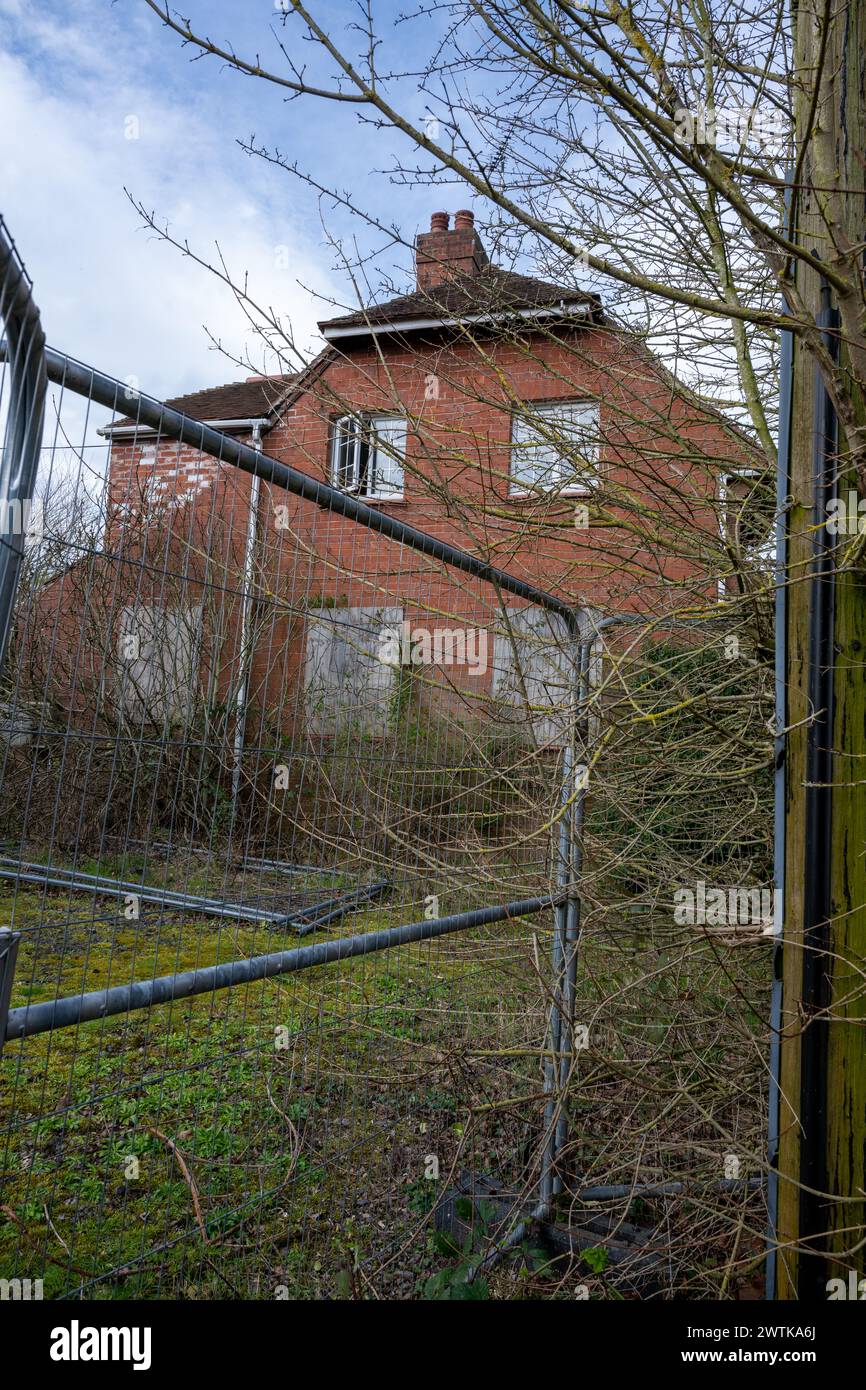 Empty and boarded up house awaiting demolition with high wire fence stopping anyone approaching the site. Stock Photo