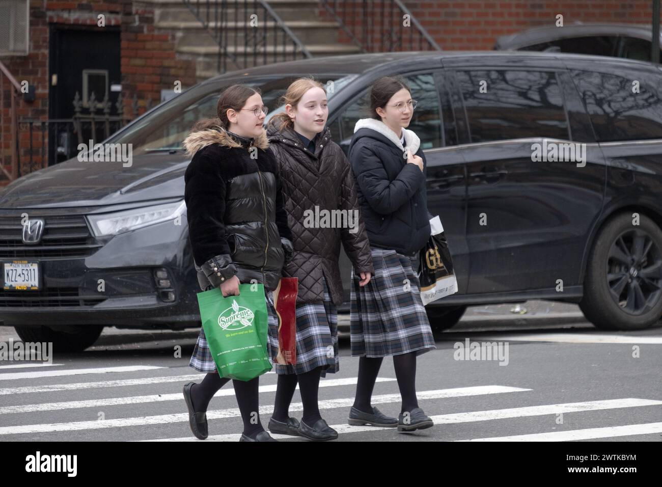 Orthodox Jewish classmates wearing the same tartan skirts cross a street in Brooklyn, New York. Stock Photo