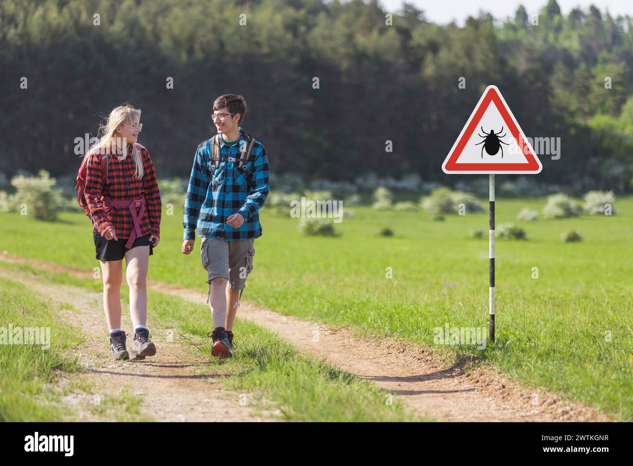 Hikers walking past tick Infected area with danger sign. Risk of tick