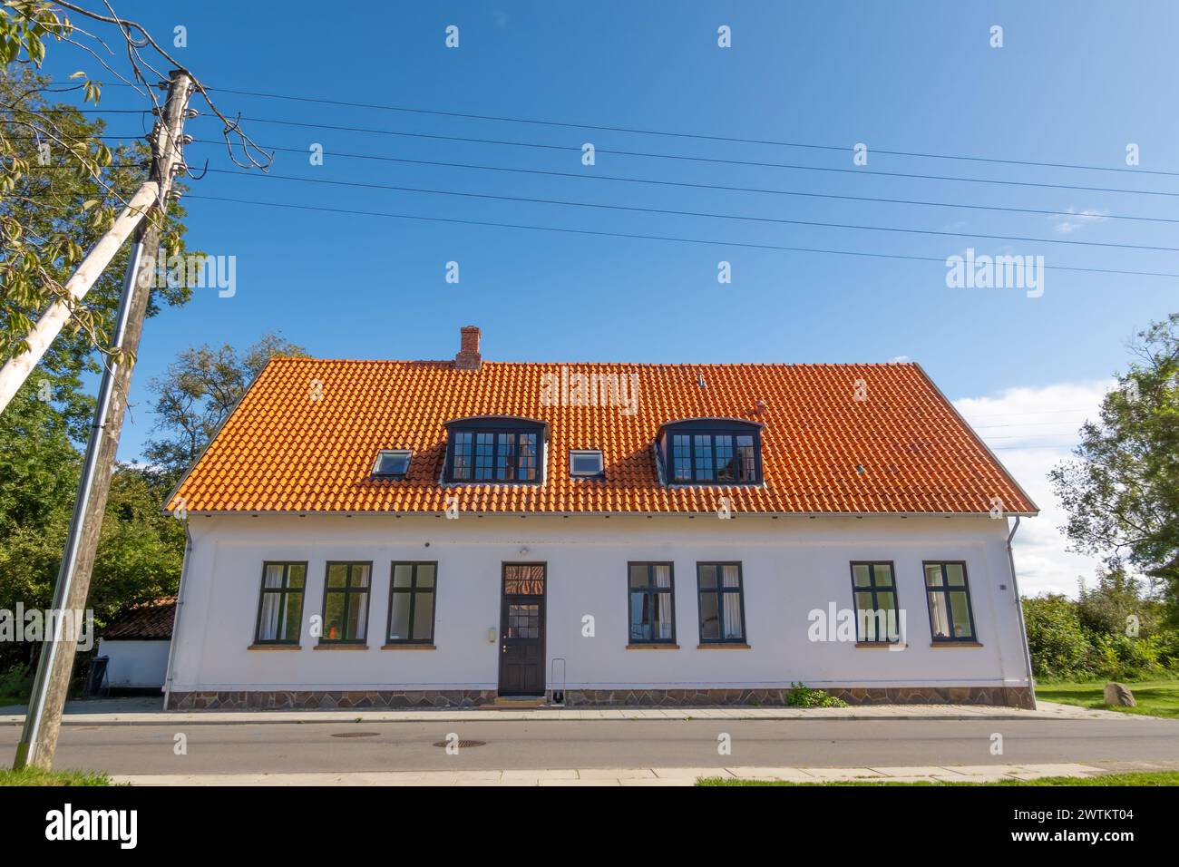White house with red roof tiles and overhead electricity wires along the street on Livø island, Limfjord, Nordjylland, Denmark Stock Photo