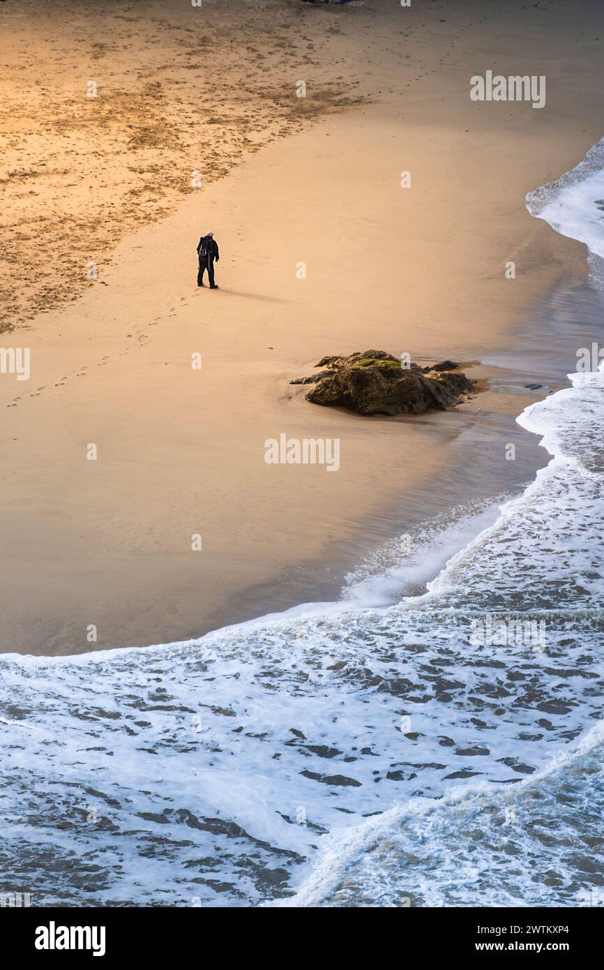 Evening light over a single figure walking across Great Western Beach in Newquay in Cornwall in the UK. Stock Photo