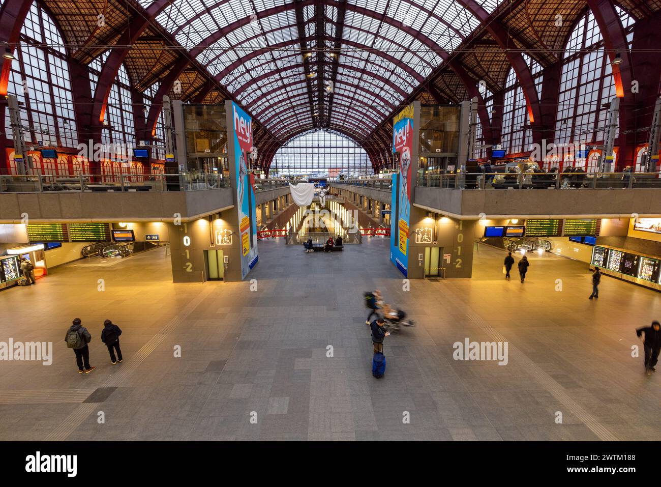 Antwerp, Belgium, January 25th, 2024, This photograph offers a view of the expansive interior of Antwerp Central Station, capturing the grandeur of its arched red ceiling and the spaciousness of its main concourse. Passengers appear scattered throughout, some in motion and others standing still, against the backdrop of shops and information displays. The station's design, which seamlessly integrates historic architecture with modern functionality, serves as a central hub for travelers from around the world. Expansive Interior of Antwerp Central Station. High quality photo Stock Photo