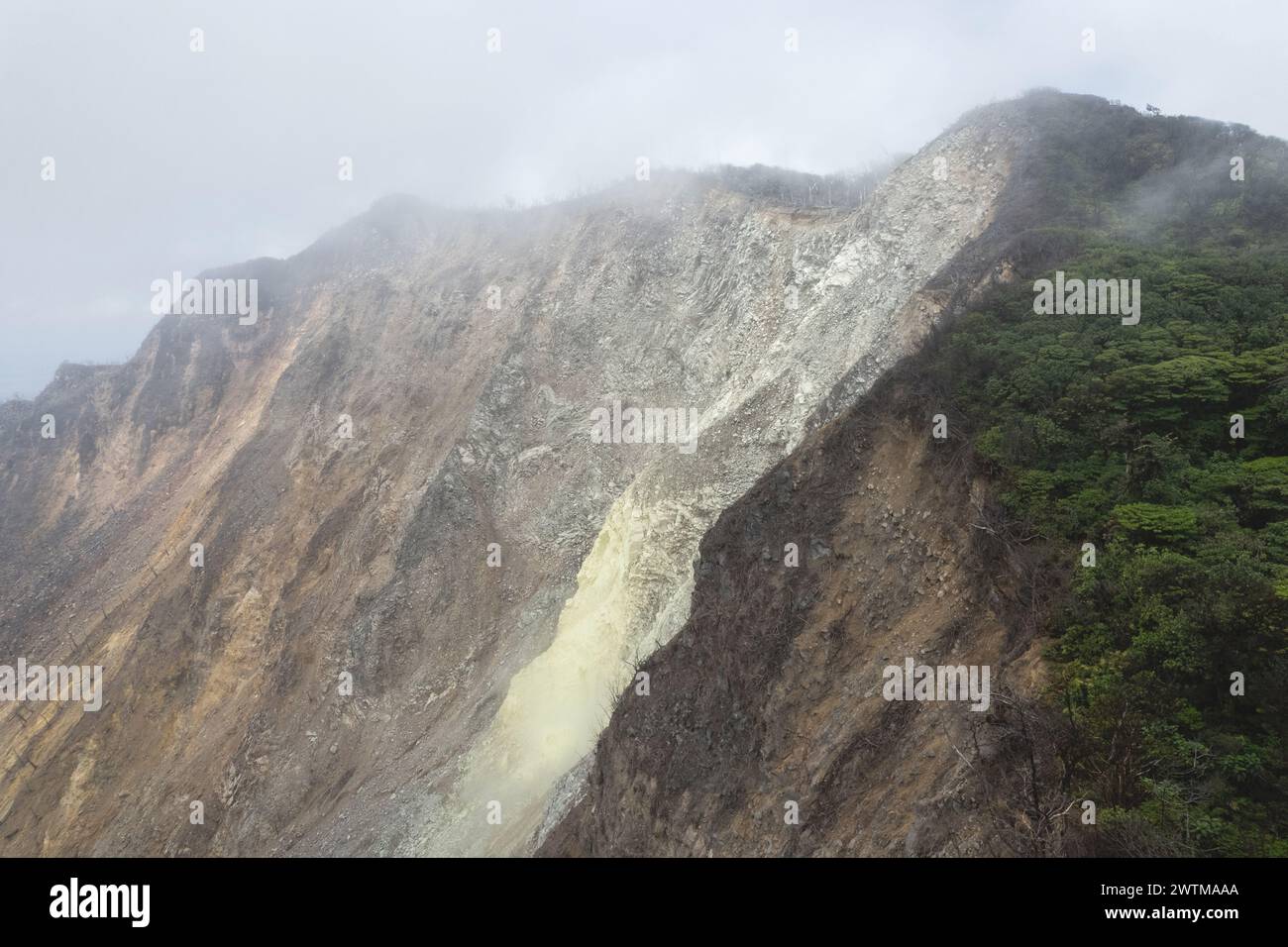 Volcano crater with yellow sulfur slope in smoke cloud sky Stock Photo
