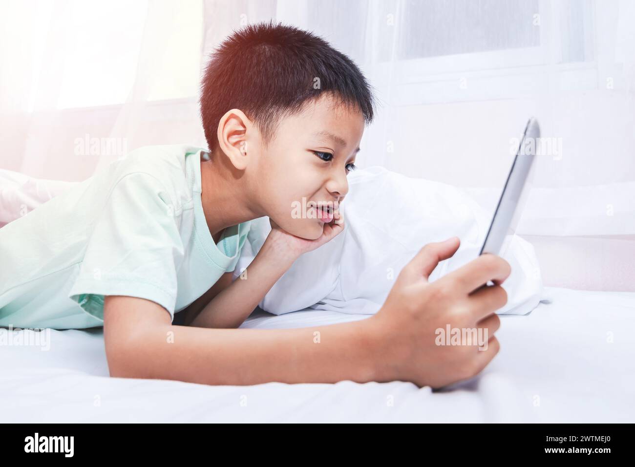 little boy looking at a tablet and playing games while lying on the bed ...