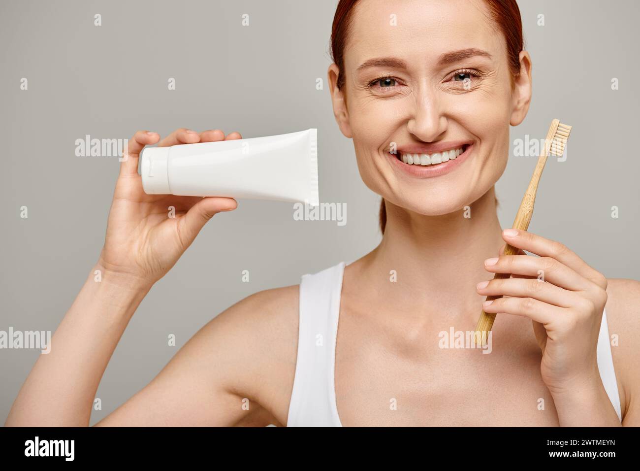 happy woman with red hair holding toothpaste and toothbrush and smiling